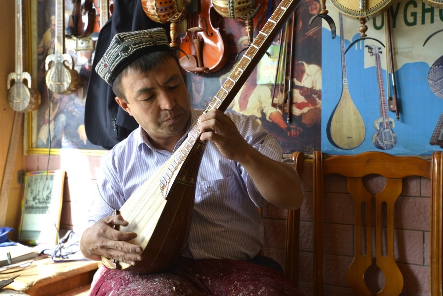 The picture shows a Uyghur instrument maker in Xinjiang, crafting a traditional musical instrument, the dutar. 